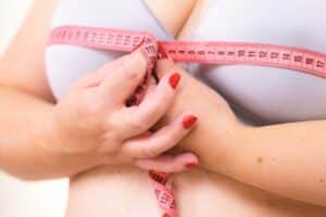 Close-up of a woman in a bra using a measuring tape to assess her chest size, illustrating breast reduction evaluation and bra fitting concerns related to large breast size